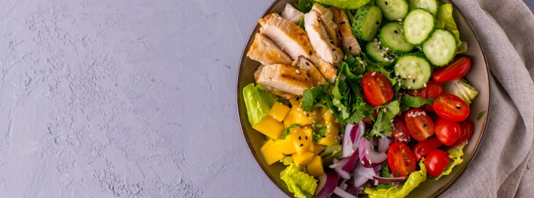 Grilled Chicken Mango Salad with cilantro, cucumbers, cherry tomatoes and red onion, top view with copy space