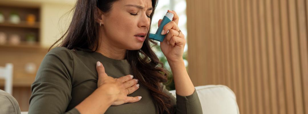 Junge Frau, die sich beim Atmen schwer tut und einen Inhalator benutzt, während sie ihre Brust hält und Asthmasymptome und Atembeschwerden zeigt.