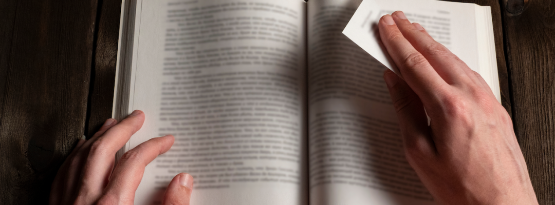 Nahaufnahme männlicher Hände, die eine Seite eines Buches auf einem dunklen Holztisch drehen. Konzept von Lesen, Literatur, Bildung, Lernen und Wissen