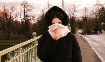 Frau mit Schal vor dem Gesicht geht über Brücke