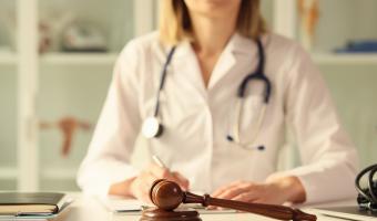 Nahaufnahme einer hölzernen Richterkavel auf einem Tisch weibliche Ärztin, die Papierkram auf dem Hintergrund macht. Rechtsstreitigkeiten, Missbräuche und kriminalistische Konzepte