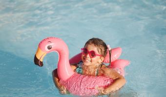 Cute funny toddler girl in a sunglasses relaxing on inflatable toy ring floating in pool have fun during summer vacation. Child having fun in swimming pool.